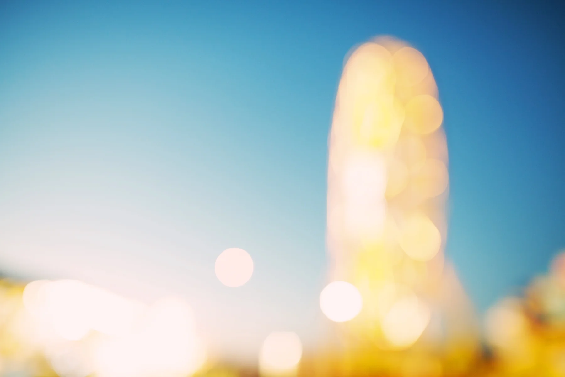 Abstract blurred bokeh lights in gold and white against a blue sky gradient